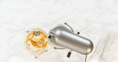 Klasik Şekerli Kurabiye Hamuru malzemeleri içeren elektrikli mikser ve kaselerin üst görüntüsü. Karıştırıcı kısmen karışık malzemelerle bir kasenin üzerine yerleştirilirken, yakındaki kaselerde un ve...