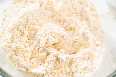 Klasik Şekerli Kurabiye Hamuru için, un ve şeker içeren kuru malzemelerle dolu bir karıştırma kabının açılı görüntüsü. Kase mermer bir tezgahın üzerine kurulmuş, yakınındaki konteynırlar da diğerini tutuyor.