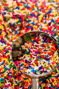 Renkli gökkuşağı parçacıklarıyla dolu paslanmaz çelik bir kepçenin makro görüntüsü. Etrafı şeker parçacıklarıyla dolu. Blog, parti temaları veya şekerci reklamları için ideal.