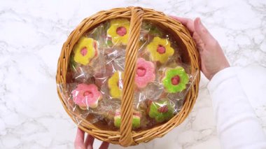 Eller paketlenmiş bir sepetten çiçek şeklinde tek bir kurabiye çıkarır ve detaylarına dikkat çeker. Ürün yakın çekimleri, pastane vitrinleri veya tatlı tanıtım içeriği için harika..