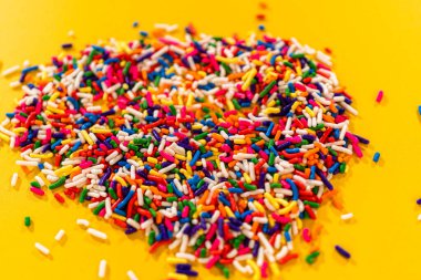 Parlak sarı bir yüzeye yayılmış canlı şeker parçacıklarının yakın çekim görüntüsü. Geçmişi, parti davetiyeleri, doğum günü temaları ya da tatlı reklamları için mükemmel..