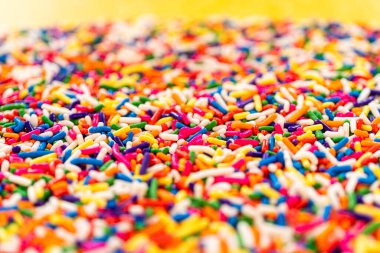 Makro renkli şeker serpintileri parlak sarı bir arka plana karşı bulanık ve canlı bir ön plan oluşturuyor..