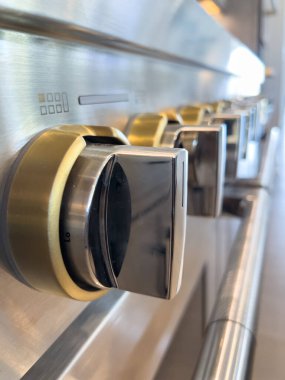 Paslanmaz bir sobanın pirinç aksanlı brülör topuzunun aşırı yakın çekimi. Makro görünüm dokuyu, materyalleri ve kesin tasarım elemanlarını vurgular.