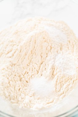Çok amaçlı un, kabartma tozu, tuz ve krema karışımı ile dolu bir cam karıştırma kabı limonlu kurabiye yapmak için çırpılmaya hazır. Kuru malzemelerin birleştirilmesi