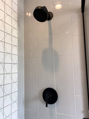 Duvara monte edilmiş kafa ve kontrol vanası da dahil olmak üzere, mat siyah armatürlerle beyaz kaplamalı temiz bir duşun dikey görüntüsü. Estetik, geometrik duvar kalıpları ile minimal ve modern..