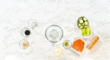 Tütsülenmiş somon ruloları için malzemeler mermer tezgahın üzerinde aralıklarla duruyor ve minimalist bir hazırlık sahnesi yaratıyor..