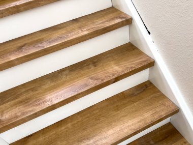 Kapalı alandaki merdivenlerde tahta taban ve beyaz basamakları gösteren dar bir ekin. Konsantrasyon, yumuşak ışıklandırma ve temiz kompozisyon ile malzeme dokusu ve bitiş üzerinde yoğunlaşmıştır..