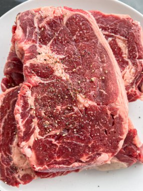 Temiz beyaz bir tabakta biberli iki çiğ pirzola bifteği. Doku ve kesik açıkça görülüyor..