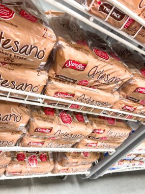 Parker, Colorado, ABD-20 Haziran 2025 - Metal market raflarına istiflenmiş paketlenmiş zanaatkar ekmek somunlarının yakın görüntüsü. Ekmek markası ve etiketleri bir depoda açıkça görülüyor.