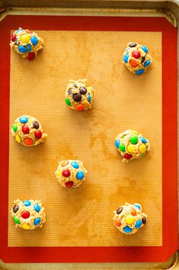 Parker, Colorado, ABD-1 Temmuz 2025 üzerinde renkli çikolata şekerleri bulunan çiğ kurabiye hamuru toplarıyla dolu bir tepsinin yukarıdan aşağı görüntüsü. Kurabiyeler silikon bir hasırın üzerine yerleştirilmiş..