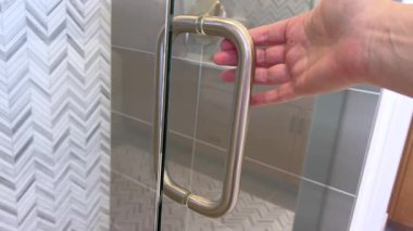 Paslanmaz çelik duş kulpu ve fayanslı duvarın yakın çekimi. Sembol deseni büyük gri fayanslarla çelişiyor.