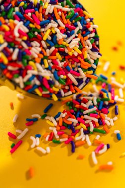 Sıkıca kırpılmış makro şeker parçacıkları metal bir kepçeyle üst üste yığılmış, canlı ışıklandırmayla sarıya yerleştirilmiş..