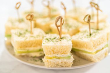 Yumuşak beyaz ekmekten yapılmış küçük çay sandviçleri krem peynirle kaplanmış ince dilimlenmiş salatalık ve taze dereotla kaplanmış. Her sandviç bambu kokteyli ile korunuyor ve servis ediliyor.