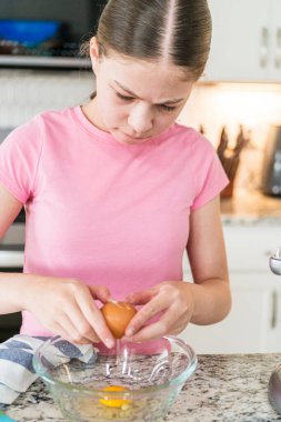 Bir kız mutfak tezgahında duruyor ve karışıma malzemeleri karıştırmaya hazırlanıyor. Pembe bir gömlek giyiyor ve arka planda bir soba, fırın ve diğer mutfak aletleri var..