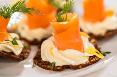 Çıtır bir krakerin üzerine zarif bir şekilde yerleştirilmiş füme somon kanalı. Üstünde krem peyniri, taze kekik ve zeytinyağı var. Canlı portakal somonu kontrastları