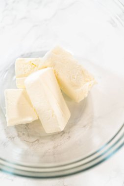 Yumuşak tereyağını yakın plan bir küp haline getirip mermer bir tezgahın üzerindeki cam karıştırma kabına yerleştirdim. Bakış açısı kremsi dokuya net bir bakış sağlar, bu da onu pişirmek ve pişirmek için ideal kılar.