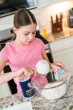 Parker, Colorado, ABD-1 Temmuz 2025 - Genç bir kız bir ölçü kabından granit bir tezgahın üzerine temiz bir cam karıştırma kabına un döküyor. Mutfakta modern aletler ve rahat, temiz