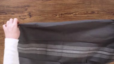 Gri çizgili bir mutfak havlusu ahşap bir yüzeye düzgünce konur, her iki elinde iki eliyle. Bileşimi simetrik ve hareketsiz..