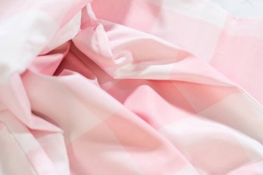 Pembe bir tekstil kumaşında köşegen kıvrımlar. Damalı desen ve yumuşak vurgular kumaş dokusunu ve ışık yansımasını vurgular.