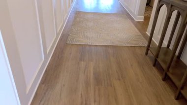 Açık ahşap zemin, beyaz duvarlar ve bej bir halının olduğu geniş bir koridor açısı. Sahne sakin ve temiz bir atmosferi çağrıştırıyor..