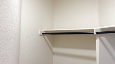 Siyah metal bir çubuk, beyaz bir rafın altına, gömme dolaba monte edilir. Resim işlevsel ve modern depolama çözümlerini vurgular.