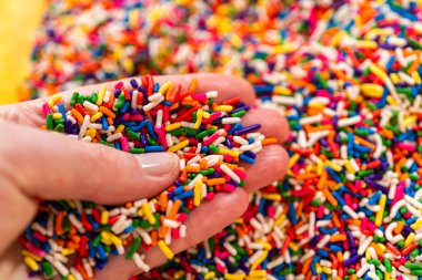 Renkli gökkuşağı parçalarını serpiştirilmiş arka planda nazikçe tutan bir elin yakın çekimi. Yemek blogları, şeker reklamları veya tatlı temalı tasarımlar için idealdir..