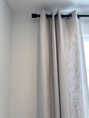 Işıl ışıl bir iç mekanda siyah bir perde çubuğundan sarkan bej kumaş perdeler..