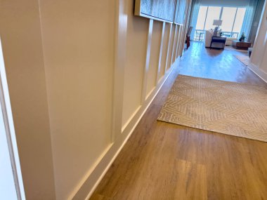 Uzun bir mesken koridorunda aksan duvarı süslemesi, ahşap döşeme ve tarafsız bir halı bulunur. En uçta, büyük bir pencere doğal gün ışığı getirir..