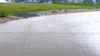 Yakın zamandaki bir yağmur fırtınasından sırılsıklam olmuş geniş beton bir veranda ve kenar boyunca su toplanıyor. Sahne, modern evleri ve peyzajı olan bir yerleşim bölgesinde geçiyor..