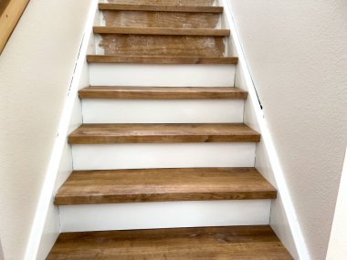 İç merdiven, orta tonda ahşap lastik izleri, temiz beyaz süslemeler, kafa kafaya. Işıklandırma yumuşaktır, mekanı sıcak ve modern hissettirir..