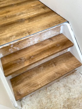 Görüntü, yeni laminatla döşenmiş üç kapalı merdiven basamağının yakın görüntüsünü yakalar, yan süsleme açıkta kalır. Doğal renkler, temiz ve sessiz sahnelere hakim..