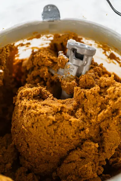 Karıştırma kabındaki koyu, koyu renkli zencefilli kurabiye hamurunun yakın çekimi, yoğun ve iyi harmanlanmış dokusunu gösteriyor. Hamur, bir sonraki yuvarlanma ve kesme adımları için hazır.