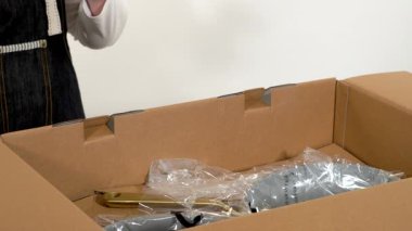 Parker, Colorado, ABD-6 Mayıs 2025 - Bir kadın karton bir kargo kutusunun içindeki plastik bir seramik tavayı dikkatlice açıyor. Sahne kapalı alanda boks yapmaya odaklandı.