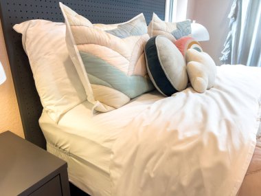 Beyaz çarşaflı modern bir yatak çeşitli renklerde yumuşak yastıklarla süslenir. Oda tasarımı rahat, şık ve çağdaş..