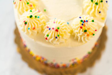 Üstten aşağıya vanilyalı pasta sergilenen renkli serpiştirilmiş, her biri renkli olan, borularla süslenmiş pembe bir manzara. Beyaz pasta yüzeyi tek tip dekorasyonla pürüzsüzdür. Görüntü net ve dengeli..