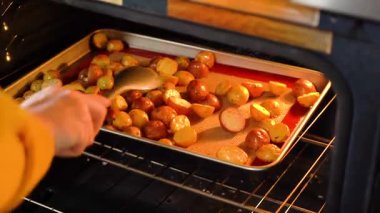 Modern bir mutfak ortamında, genç bir adam şu anda fırında baharatlı gökkuşağı patatesi kızartılarak lezzetli bir yemeğe doğru önemli bir adım atıyor..