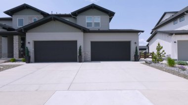 Çift katlı bir banliyö evi tarafsız dış tonlara ve büyük beton bir garaj yoluna sahiptir. Güneşli bir günde yakalanan bu görüntü, sakin yerleşim ortamını gösteriyor..