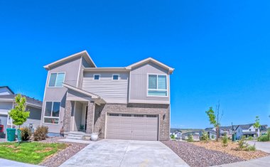 Tarafsız bir dış görünüşü ve temiz hatları olan, güpegündüz çekilmiş iki katlı bir ev. Peyzajlı ön bahçe ve geniş garaj yolu çift katlı bir garaja çıkıyor. Çevredeki evler görülebiliyor