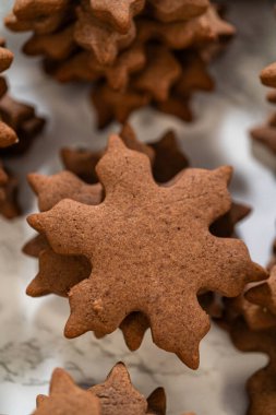 Çikolatalı zencefilli kar taneli kurabiyelerin yan görünüşü parşömen kaplamalı bir yüzeye yığılmış, festival tasarımlarını ve tatil cazibelerini sergiliyor..