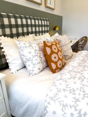 Parlak yatak odasının içinde kareli yeşil bir yatak başlığı, çoklu fırlatma yastıkları ve çiçek desenli hafif yatak desenleri var..