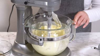 Bir karıştırıcı mermer tezgahın üzerindeki cam kasede kremalı kurabiye hamuru tutar. Parlak ışık, temiz bir mutfak ortamındaki pürüzsüz karışımı vurgular..