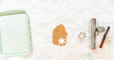 Overhead view of amber gingerbread dough alongside a green baking tray, cookie cutters, and a rolling pin, ready for shaping into snowflake cookies.
