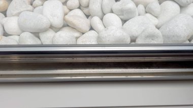 Close-up of a window well with a view of smooth white landscaping rocks pressed against a metal frame. The clean lines create a minimalist outdoor look.