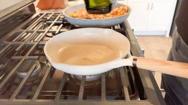 A ceramic frying pan with wooden handle is preheating on a gas stove. The flame is visible underneath as part of breakfast preparation.