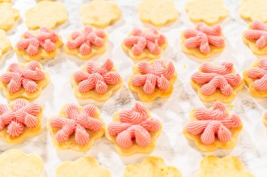 Rows of flower-shaped cookies piped with raspberry buttercream are lined up for assembling Easter Cookie Sandwiches with Raspberry Buttercream.