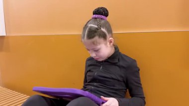 Sessiz bir koridora yerleşmiş bu genç artistik patinajcı, yaklaşan performansına zihinsel olarak hazırlanırken kendini tabletine kaptırmış bir sükunet anı buluyor..