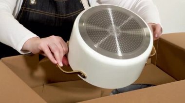 Parker, Colorado, ABD-6 Mayıs 2025 - Karton bir nakliye kutusunun üstü açık, içinde mutfak malzemesi var. Naylon ambalaj malzemesi bir kadın için hazırlanırken etrafını sarar.