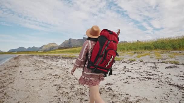 一个穿着红色大背包 头戴一顶帽子的女游客沿着山中的海滨散步 美丽的诺威夏季风景 — 图库视频影像