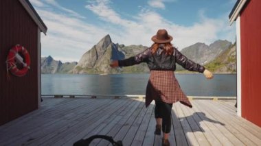 Neşeli kız, Kuzey Norveç 'teki Lofoten takımadasındaki deniz kıyısındaki geleneksel kırmızı ahşap balıkçı evinin yanındaki rıhtıma doğru koşuyor..