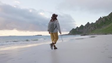 Sahilde gün batımında yürüyen tasasız mutlu bir kız. Genç, narin bir kadın deniz ya da okyanus kıyısında turist çantasıyla tek başına yürüyor ve gün batımını seyrediyor. Akşamları deniz kıyısında ya da okyanusta güneşe karşı yürümek